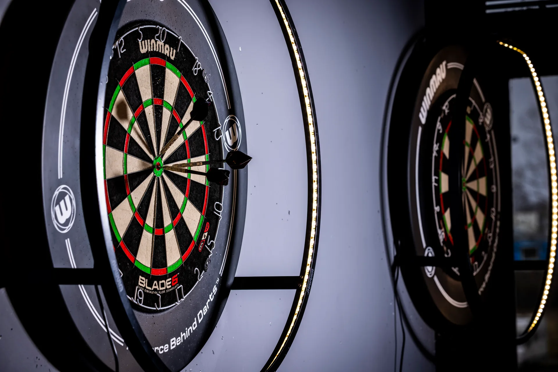 Dartsbord met drie pijlen in het midden en ingebouwde ringverlichting bij Oscars Bowling & Pool