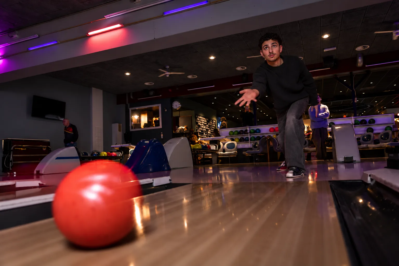 Jonge man aan het bowlen met een rode bal onder sfeervolle gekleurde verlichting bij Oscars Bowling & Pool