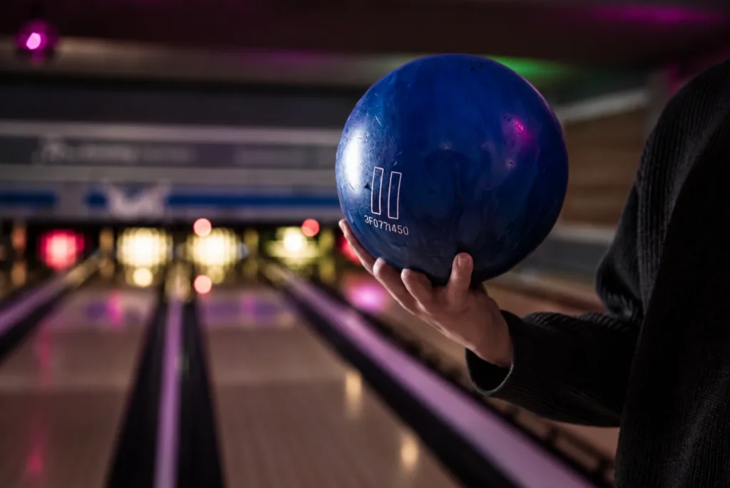 In een bowlingbaan hangt een hand met een blauwe bowlingbal klaar om gegooid te worden bij Oscars Bowling & Pool.