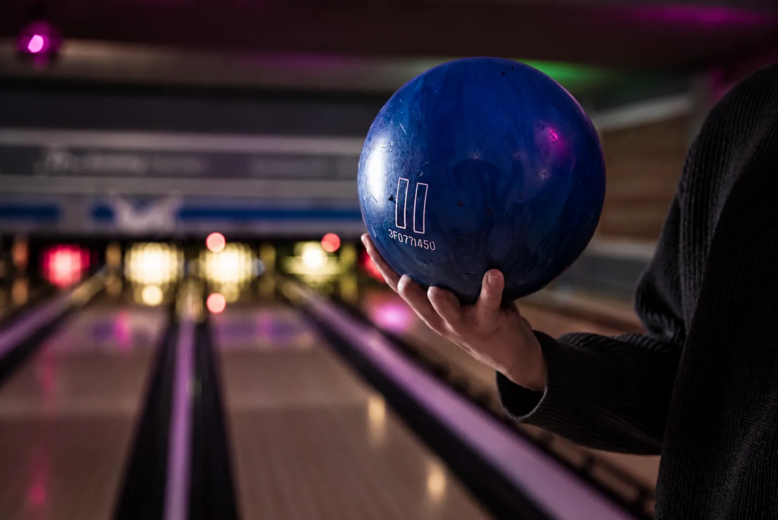 In een bowlingbaan hangt een hand met een blauwe bowlingbal klaar om gegooid te worden bij Oscars Bowling & Pool.