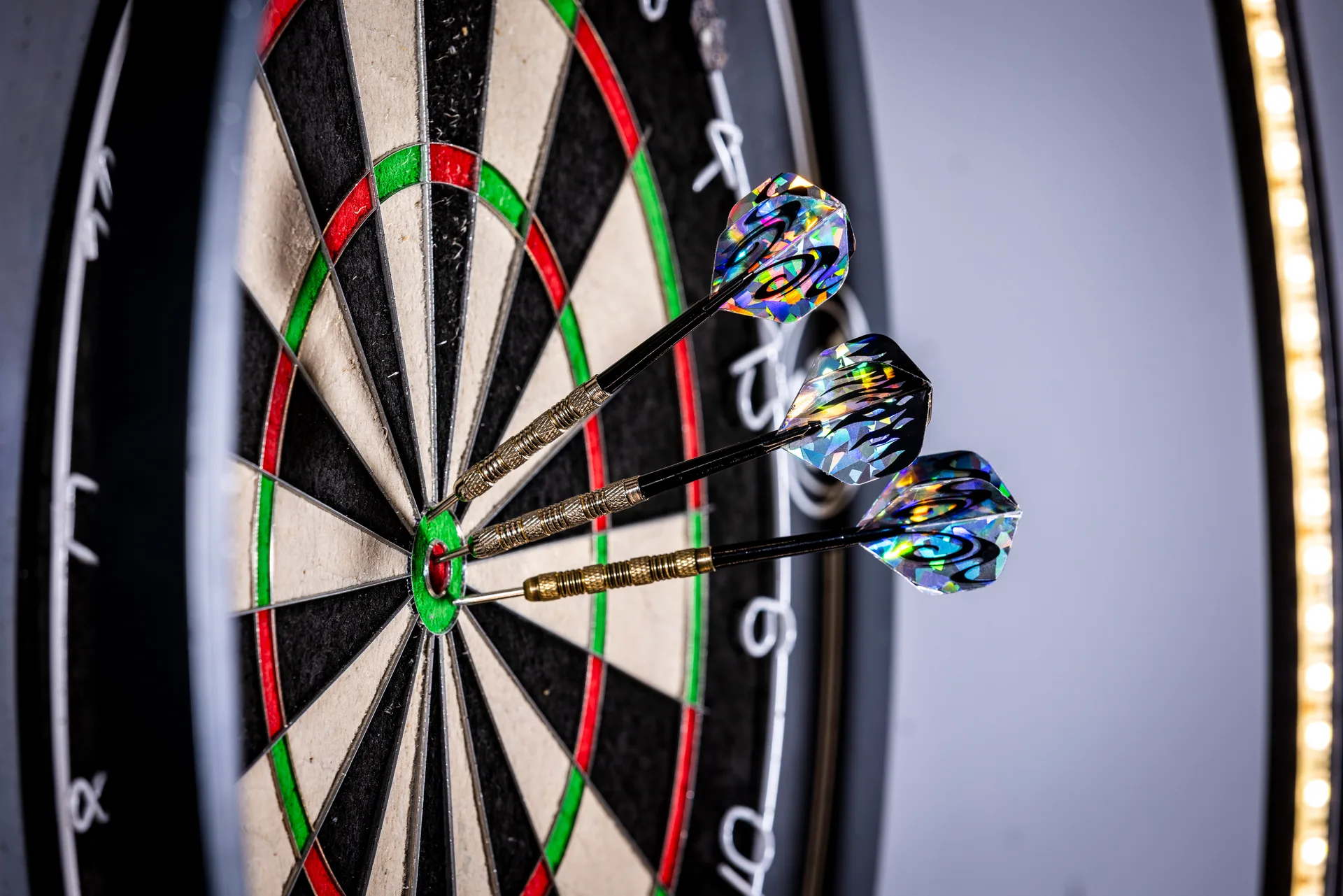 Drie darts met glanzende vluchten in het bullseye van een dartbord bij Oscars Bowling & Pool