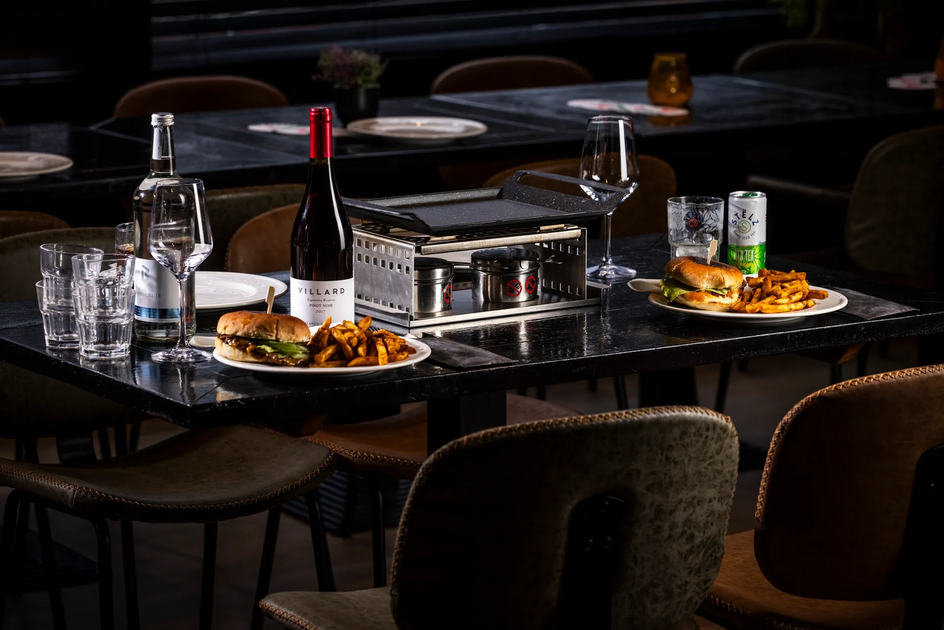 Gourmettafel met vlees en sausjes, twee borden met hamburgers en friet, een fles rode wijn, water en een blikje Stelt bij Oscar's Bowling & Pool in Zaandam