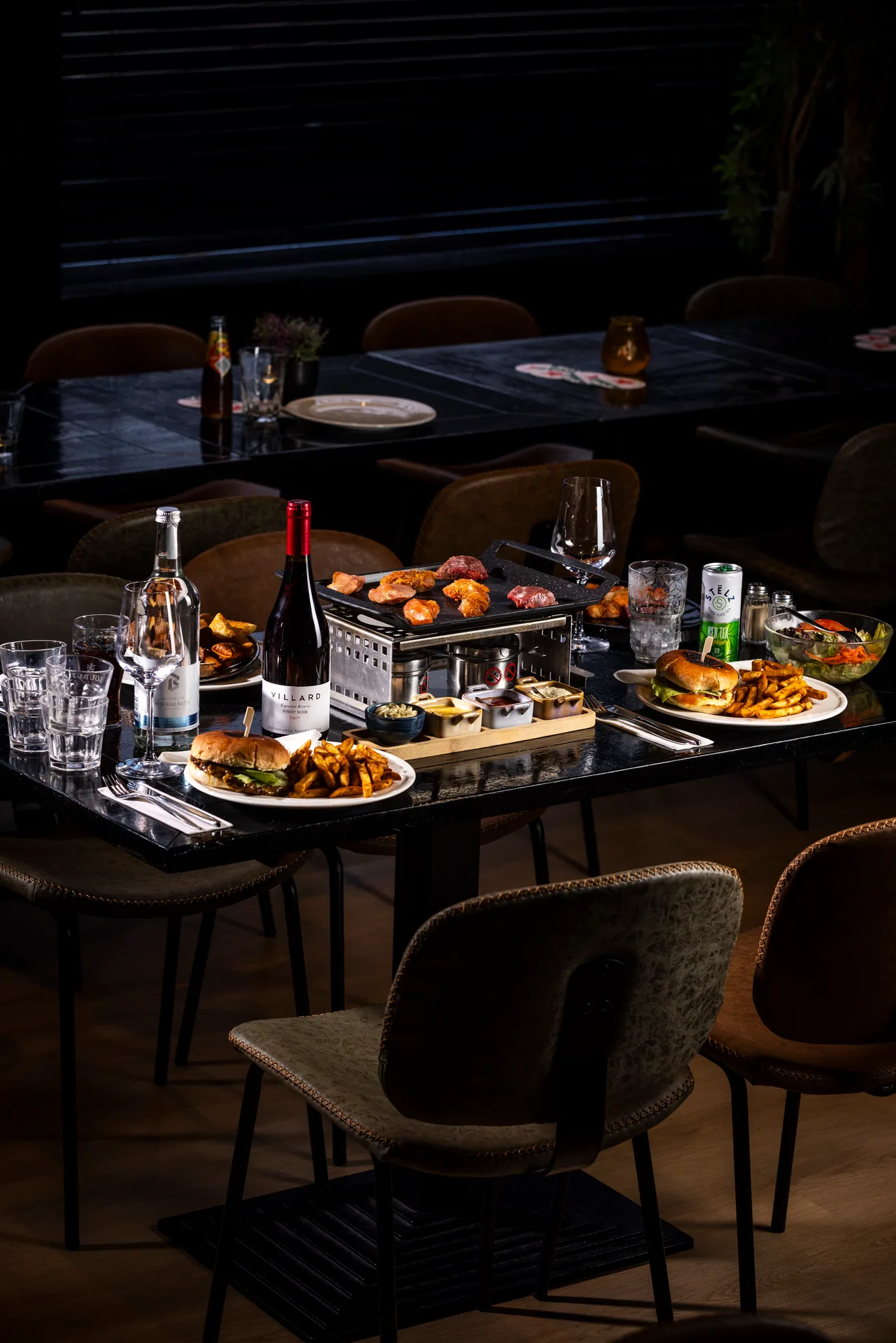 Gourmetten met vlees, burgers, friet, drankjes en sauzen op een tafel bij Oscars Bowling & Pool in Zaandam