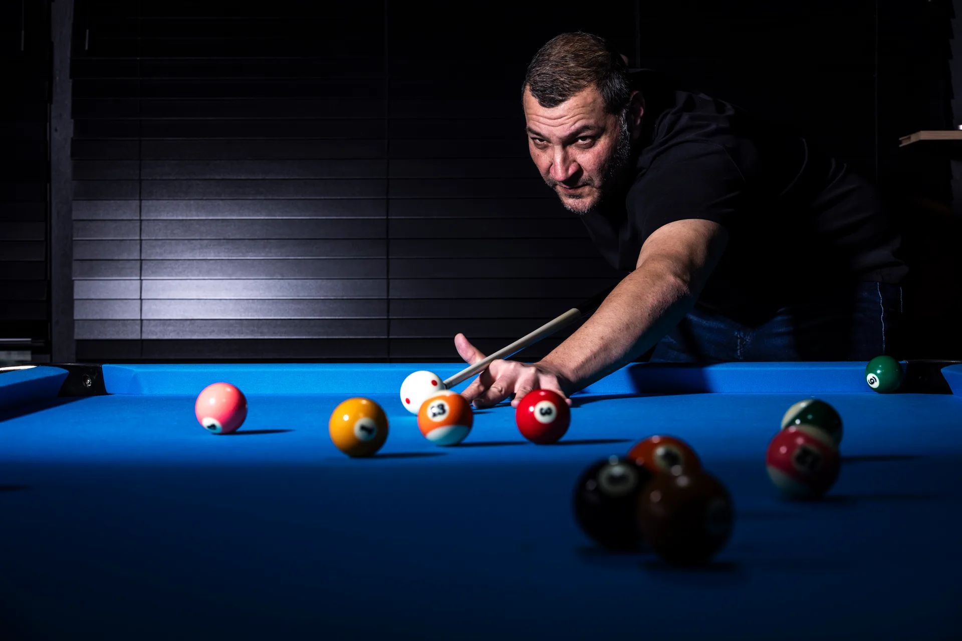 Een man speelt pool en richt met de keu op een witte bal op een blauw biljartlaken bij Oscars Bowling & Pool