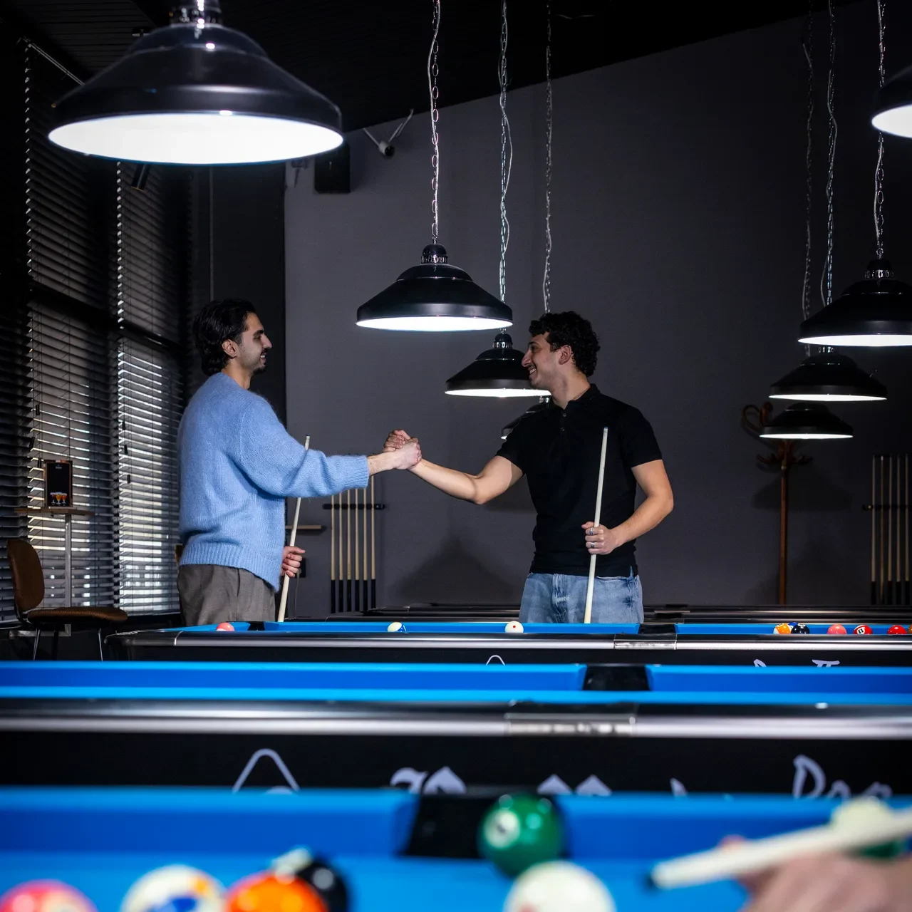 Twee mannen geven elkaar een hand bij een pooltafel in Oscar's Bowling & Pool, een poolzaal in Zaandam